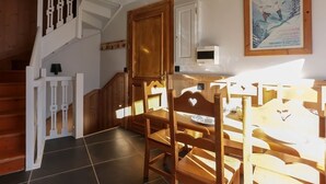 A dining area with wooden chairs and a table, a staircase with a white railing, and a poster on the wall.