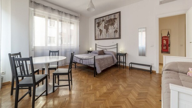 Ein Schlafzimmer mit Bett, Nachttischen, einem runden Esstisch mit Stühlen, einer Bank und einer Weltkarte als Wandbild.