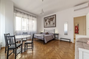 A bedroom with a bed, bedside tables, a round dining table with chairs, a bench, and a world map artwork on the wall.