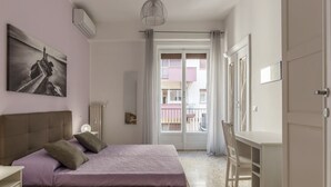 Ein Schlafzimmer mit einem Bett, einem Schreibtisch, einem Stuhl, einem Fenster mit Vorhängen und einer Wand-Klimaanlage.