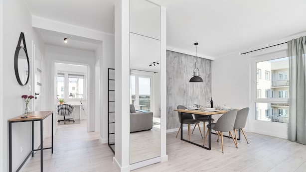 Ein moderner, offener Wohnbereich mit Essplatz, einem großen Spiegel und Blick auf die Stadt durch ein Fenster.