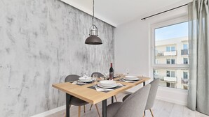 Ein moderner Essbereich mit einem Holztisch, gedecktem für vier Personen, grauen Stühlen, einer Pendelleuchte und Blick auf Gebäude durch ein großes Fenster.