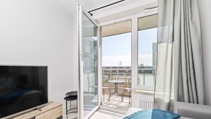 Ein modernes Wohnzimmer mit einem Flachbildfernseher, einer Couch und einer Glastür zu einem Balkon mit Sitzmöbeln.