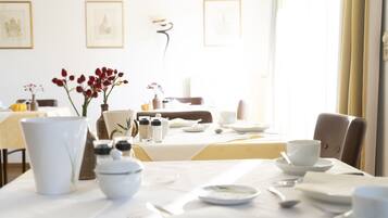 Comedor con una mesa dispuesta para dos personas, vajilla blanca y un jarrón con flores rojas.