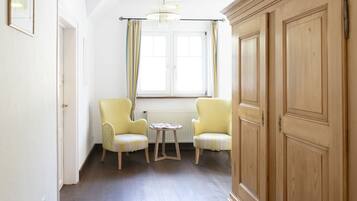 Una habitación con dos sillones amarillos, una mesa redonda pequeña, un armario de madera y una ventana con cortinas.