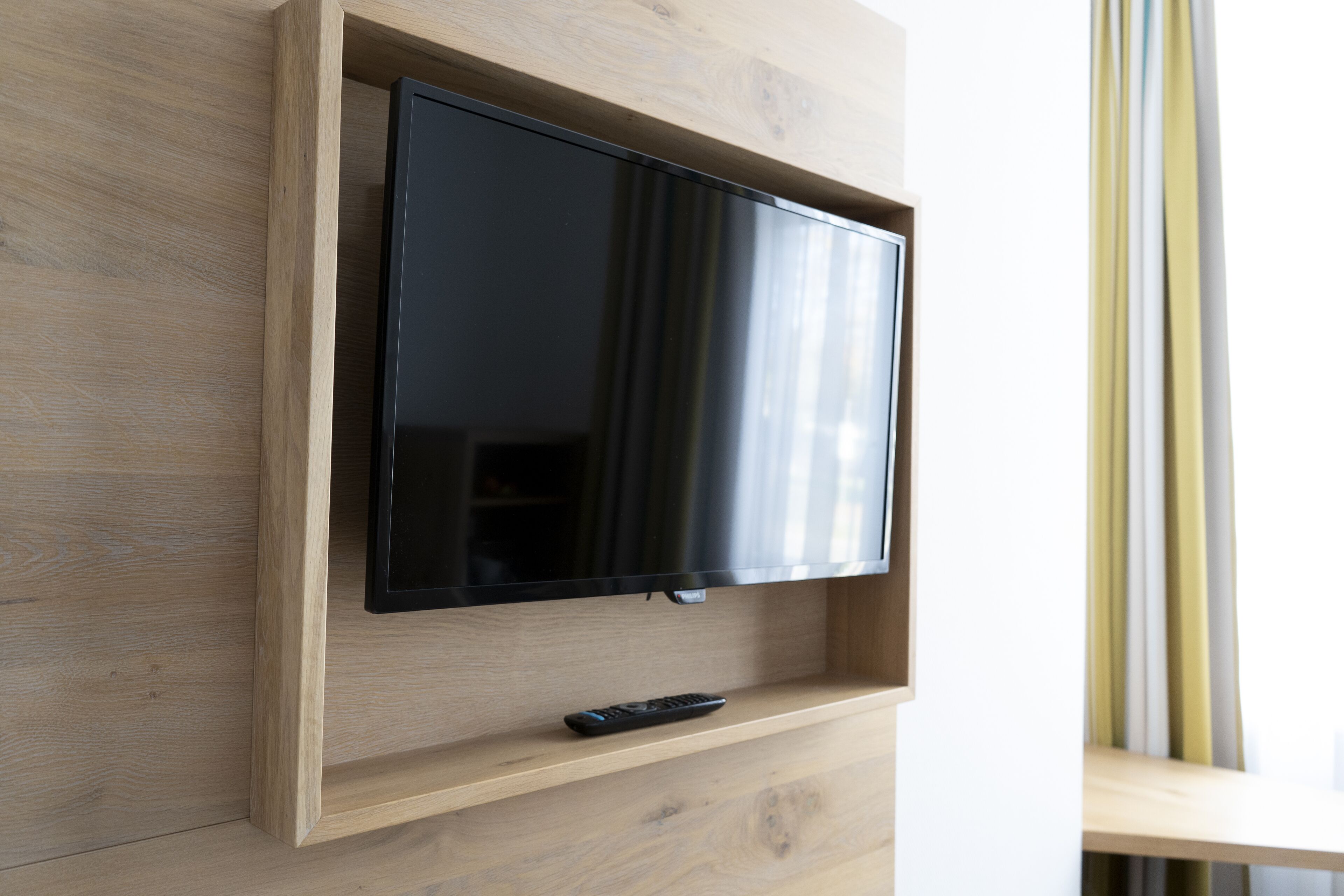 Un televisor de pantalla plana montado en una pared de madera, con un control remoto sobre un estante inferior.