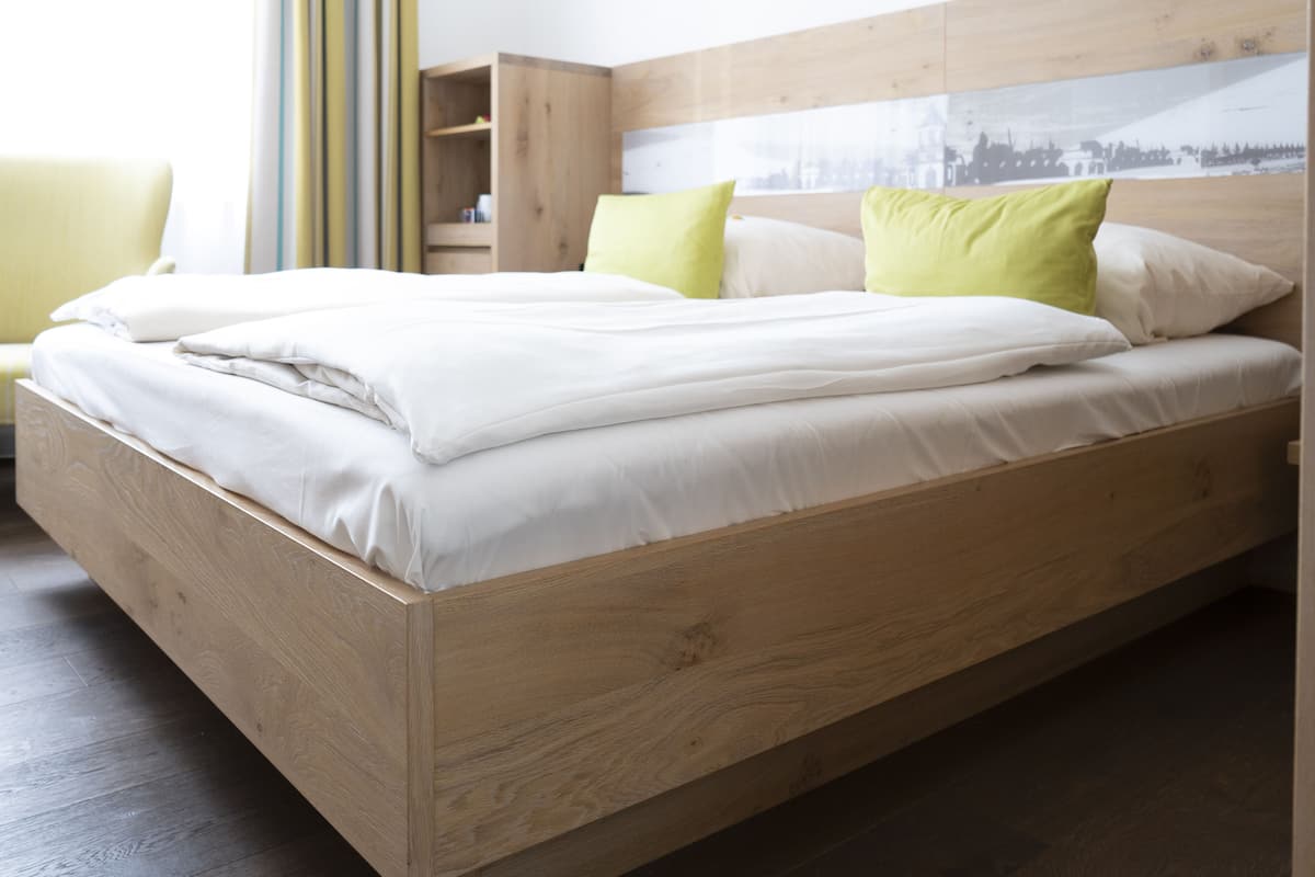 A wooden bed with white bedding and green pillows in a hotel room.