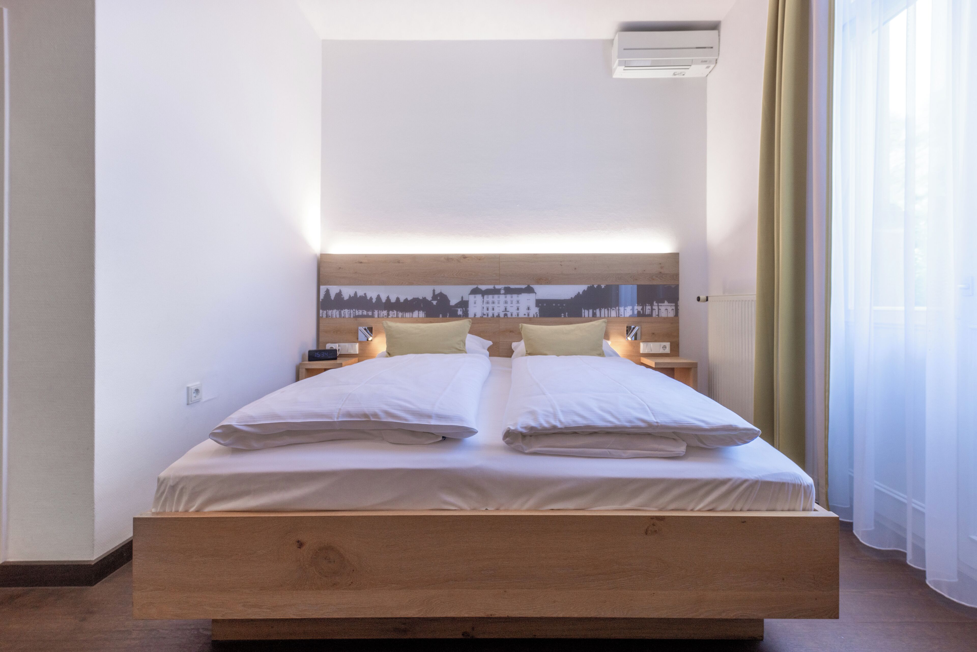 A double bed with a wooden frame, two bedside tables, and a wall-mounted air conditioner.