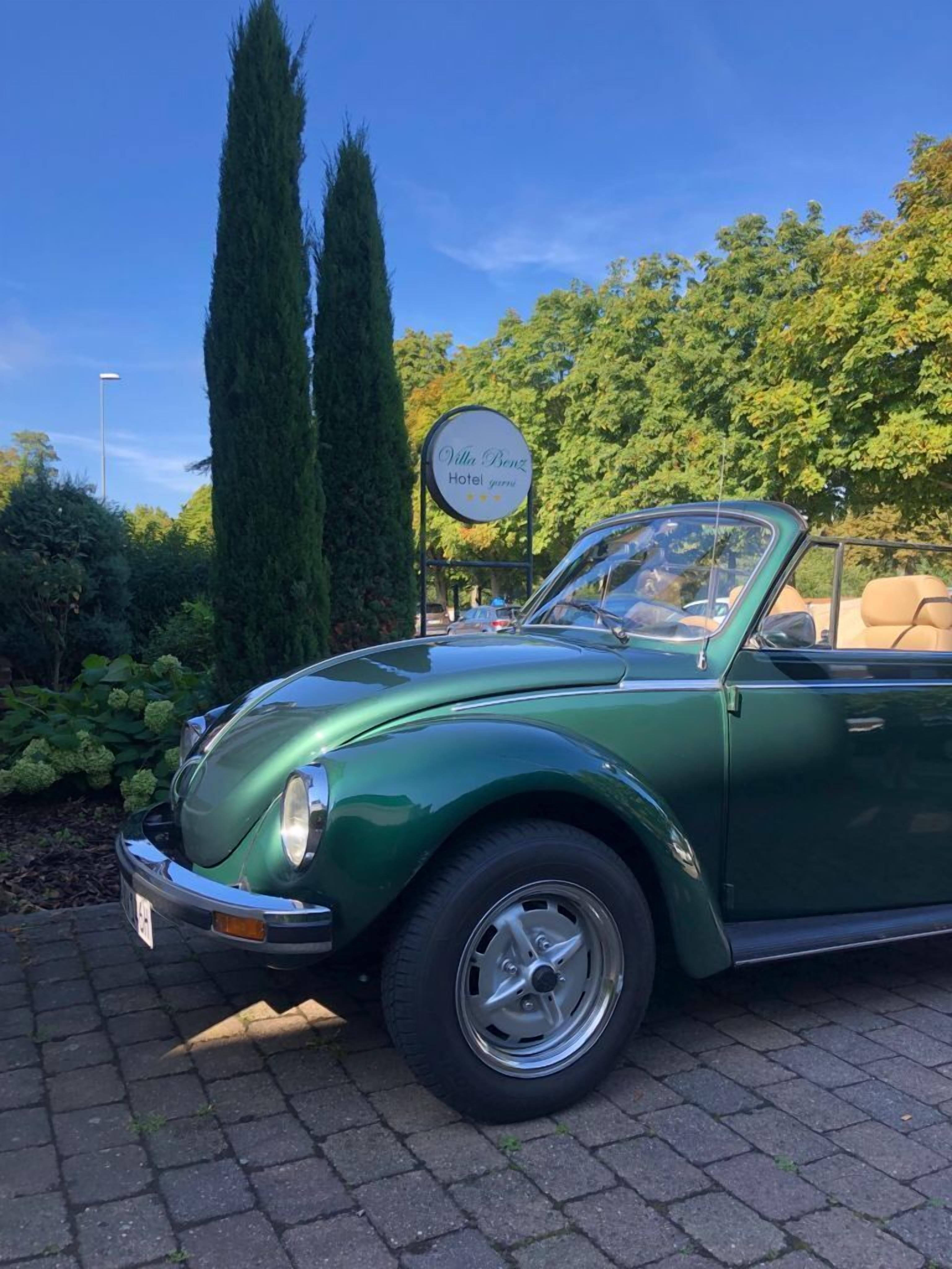 A vintage green convertible car parked in front of Villa Benz Hotel.