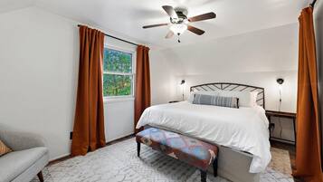A bedroom with a bed, a bench, a ceiling fan, a window, and curtains.