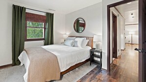 A bedroom with a bed, a bedside table, a mirror, and a window with curtains.