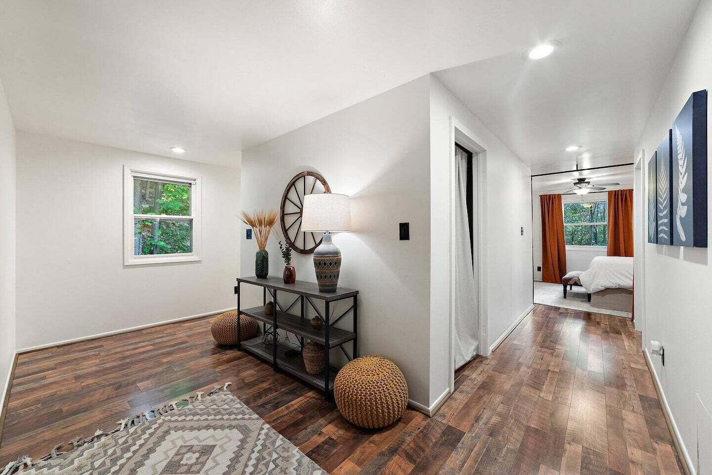 A hallway with a console table, a large mirror, and a bed in the adjacent room.