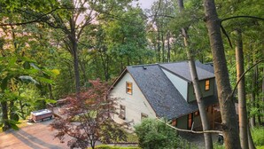 A house surrounded by dense forest, with a visible deck area and a hot tub.