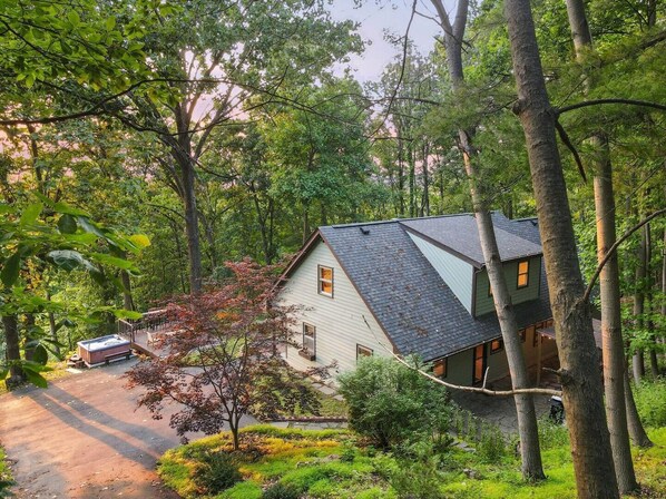 Una casa rodeada de un bosque frondoso, con un área de terraza visible y un jacuzzi.
