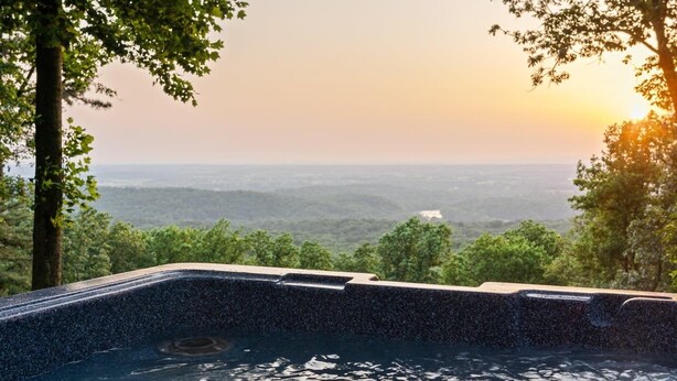 A hot tub with a view of a forested landscape during sunset.