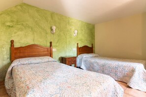 Ein Zimmer mit zwei hölzernen Betten, floralem Bettbezug, einem kleinen Nachttisch aus Holz und einer grünen Wand mit zwei Wandleuchten.