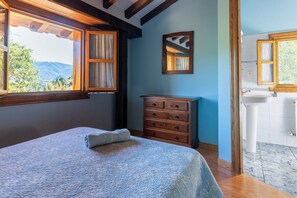 Une chambre à coucher avec un lit, une commode en bois, une fenêtre avec des rideaux et une salle de bain avec un lavabo et un miroir.