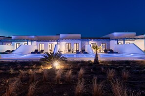 Un edificio moderno con zona de piscina, mobiliario exterior y una entrada bien iluminada.