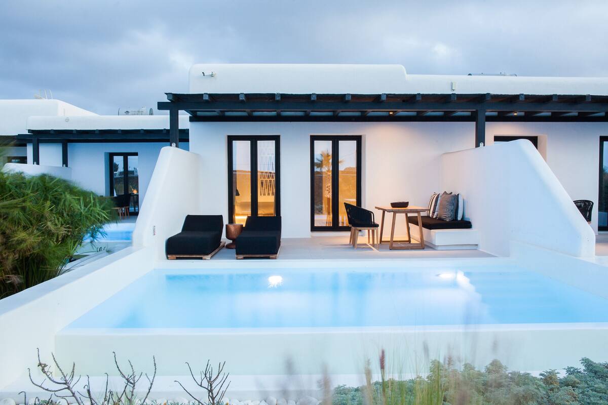Una casa moderna con piscina, mobiliario exterior y una pérgola.