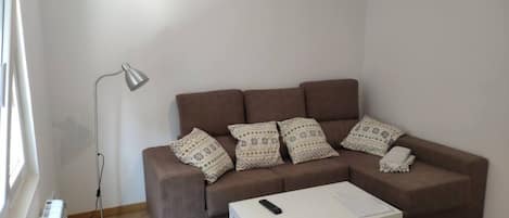 A living room with a brown sofa, patterned pillows, a white coffee table, and a floor lamp.