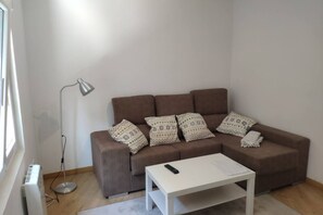 Una sala de estar con un sofá marrón, almohadones estampados, una mesa de centro blanca y una lámpara de pie.