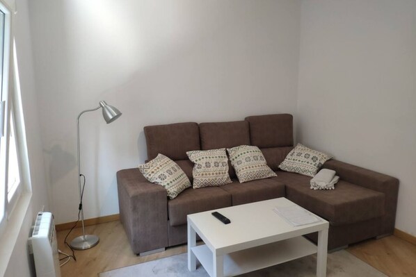 A living room with a brown sofa, patterned pillows, a white coffee table, and a floor lamp.