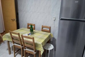 A dining area with a table covered by a checkered tablecloth, wooden chairs, a bottle, and a small round table.