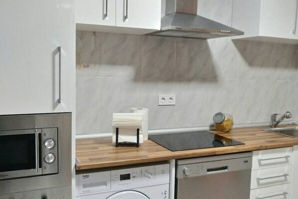 A kitchen with a built-in microwave, a dishwasher, a wooden countertop, and a stainless steel range hood.