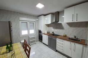 Una cocina con armarios blancos, microondas, lavavajillas y una ventana con persianas.