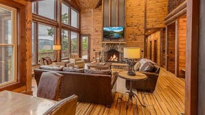 A cozy cabin interior with a fireplace, comfortable seating, and large windows offering scenic views. - Experience breathtaking mountain views at Sequoyah Sunset (Bryson City)