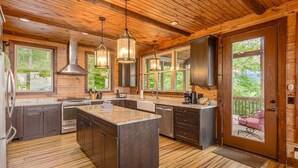 A spacious kitchen with wooden flooring, a large island, and a view of the outdoors through large windows. - Experience breathtaking mountain views at Sequoyah Sunset (Bryson City)