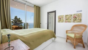 Une chambre à coucher avec un lit, une chaise en osier et une fenêtre avec des rideaux.