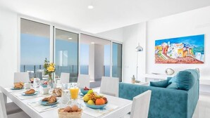 Un espace repas moderne avec une table mise pour le petit-déjeuner, un canapé bleu et un tableau représentant un paysage côtier.