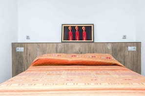 Un lit avec une couvre-lit à motifs et des oreillers, une tête de lit en bois et un tableau encadré au-dessus du lit.
