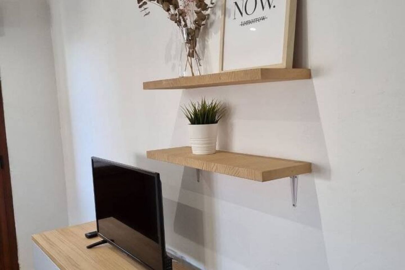 Een bureau met een computer monitor, twee houten planken met een potplant en een lijst met tekst aan de muur.