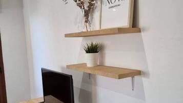 Een bureau met een computer monitor, twee houten planken met een potplant en een lijst met tekst aan de muur.