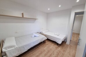Habitació petita i neta amb dos llits individuals, un terra de fusta i una paret blanca.