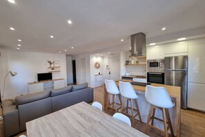 A modern kitchen with a dining area, a sofa, and a TV.