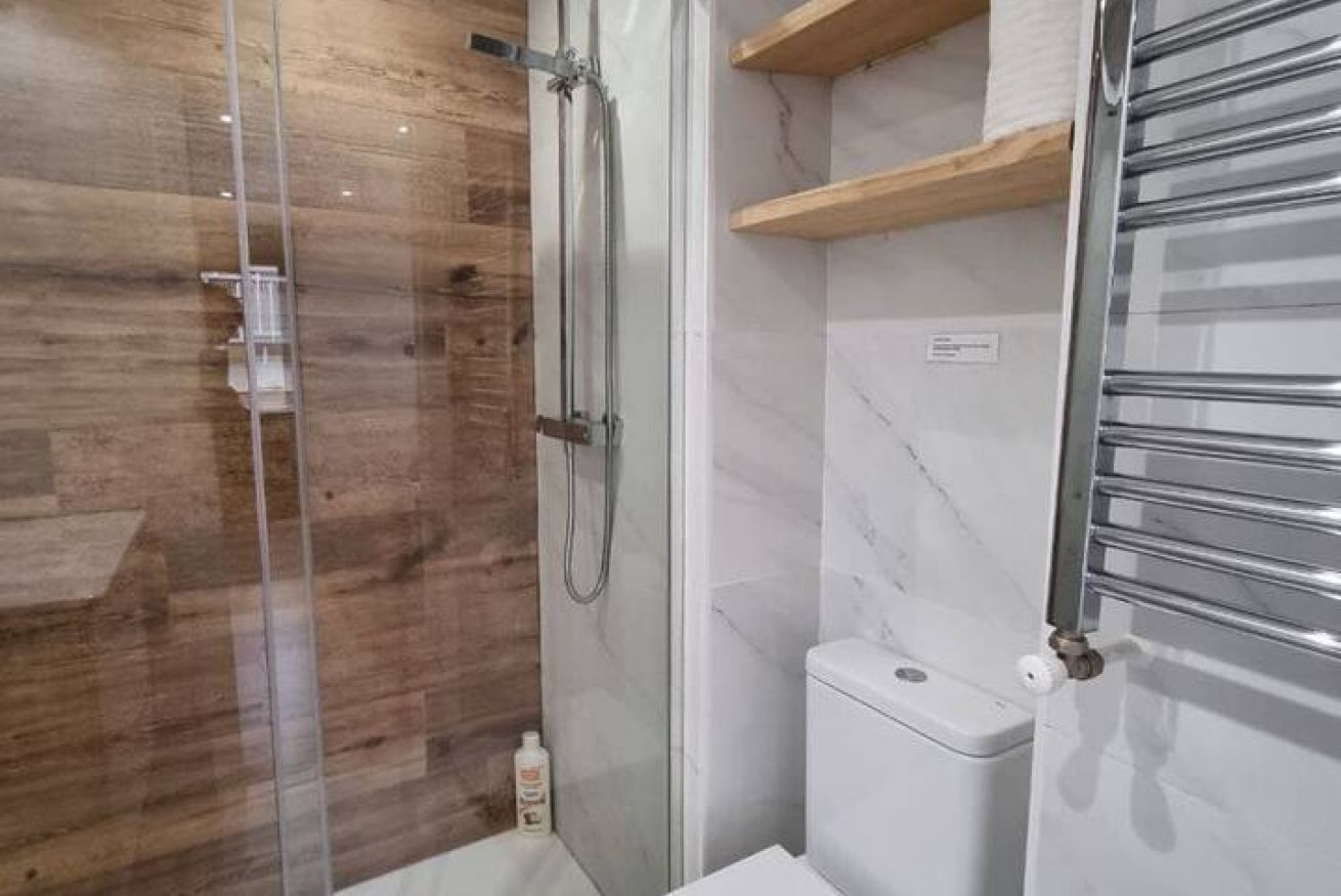A bathroom with a glass-enclosed shower, a toilet, and a metal towel rack.