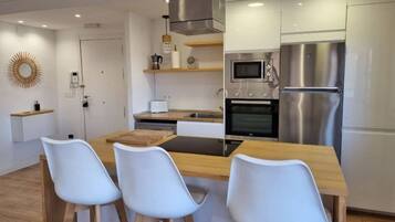 Een moderne keuken met een centraal eiland, witte stoelen, roestvrijstalen apparatuur en een houten eettafel.
