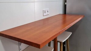 A wooden table with a white base, positioned against a white tiled wall with a power outlet. - 103A By R2R 2-Bedroom Apartment (Gijón)