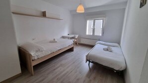 A bedroom with two beds, a desk, a chair, a hanging light fixture, and a window. - 103A By R2R 2-Bedroom Apartment (Gijón)