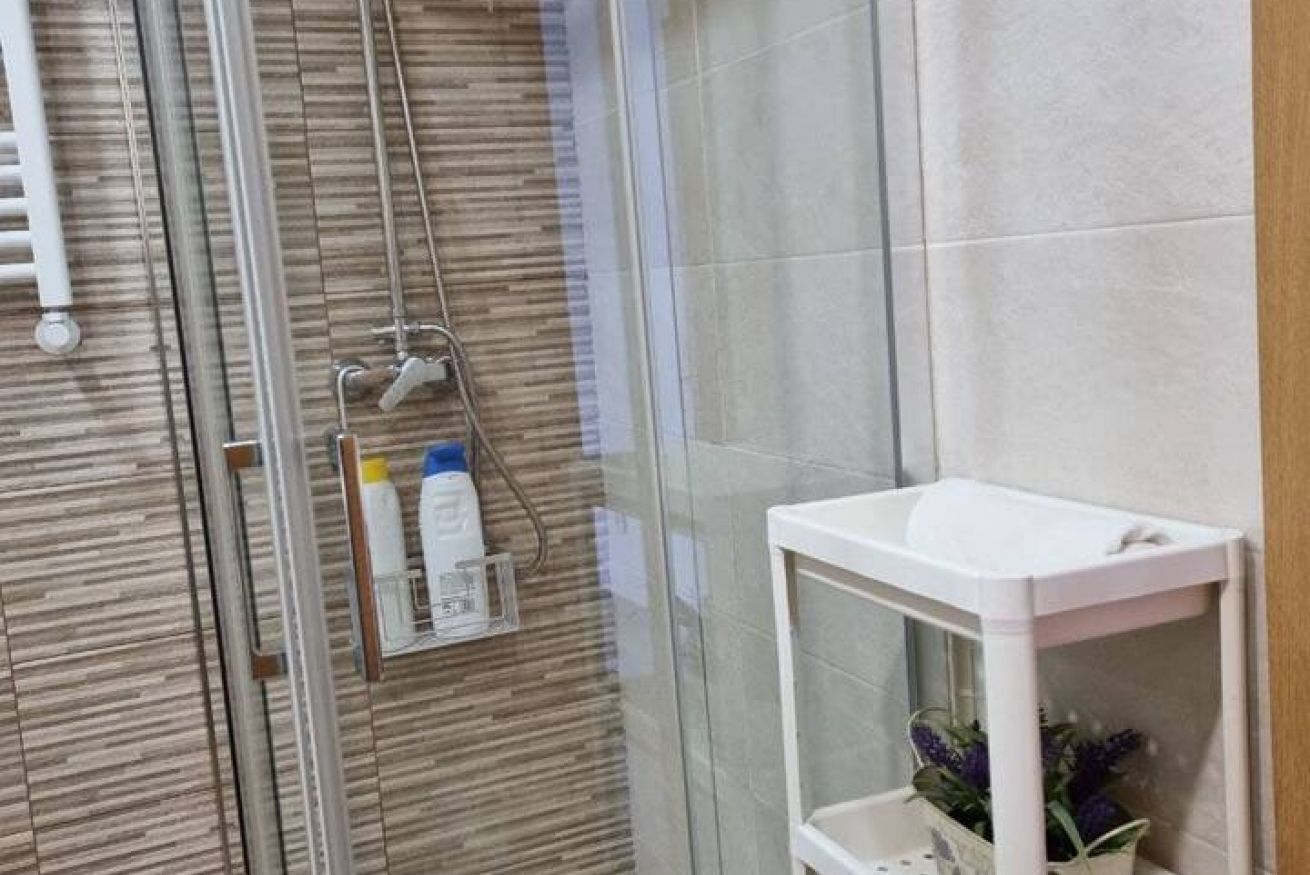 A glass-enclosed shower with a white sink and a shelf with toiletries.