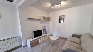 A modern living room with a flat-screen TV, a small white table, a beige sofa, and a wooden floor. - 103A By R2R 2-Bedroom Apartment (Gijón)