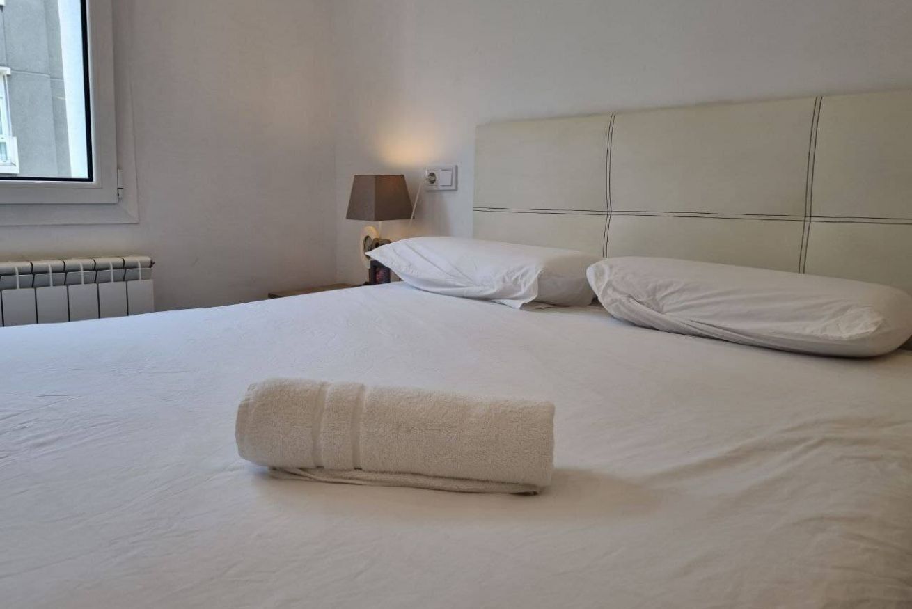 Et hotelværelse med en seng, et sammenrullet håndklæde, et natbord med en lampe og et vindue.