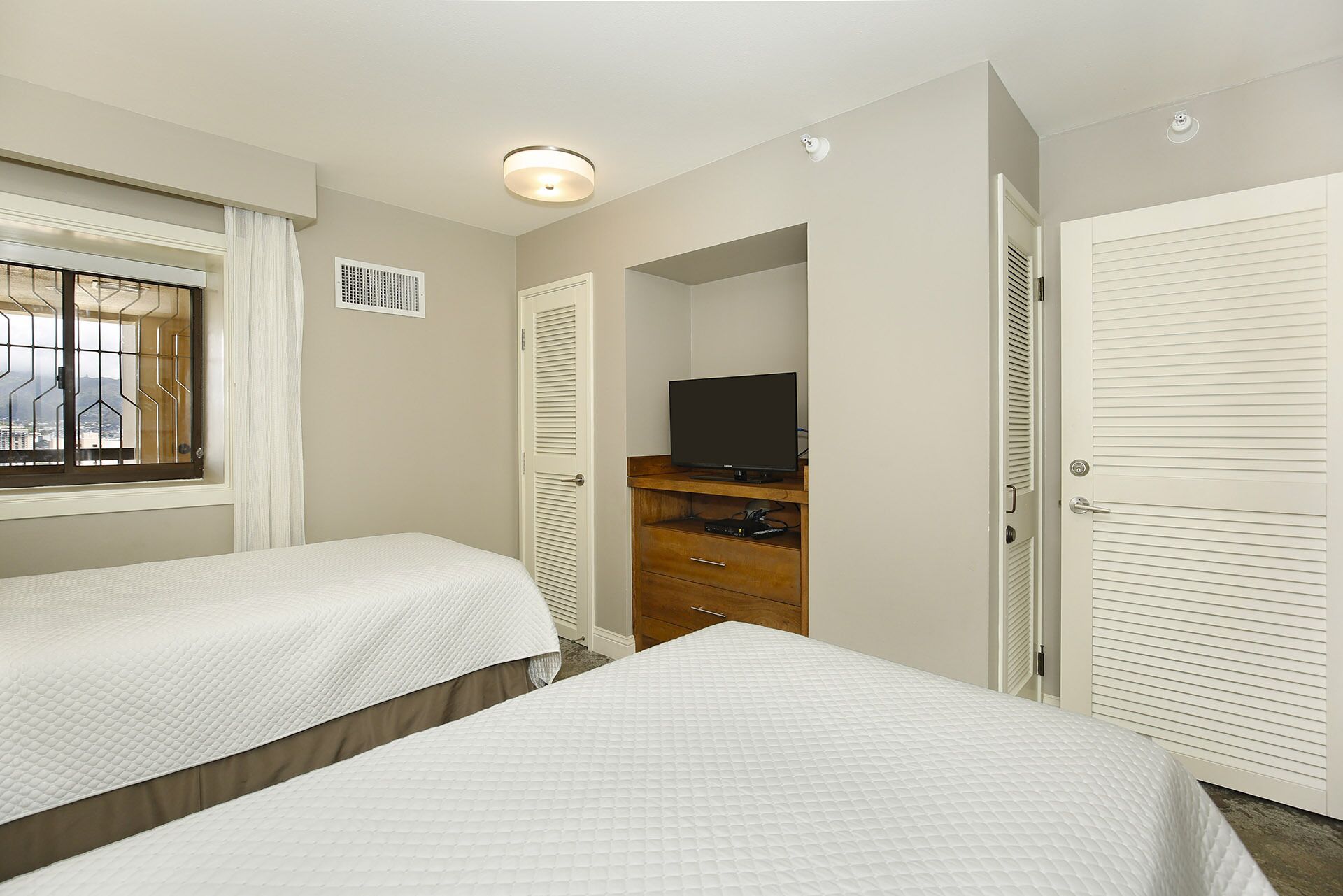 A bedroom with two beds, a TV on a wooden stand, and a window with a view.
