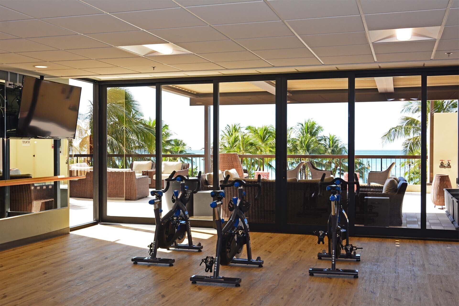 Un gimnasio con bicicletas estáticas, ventanas amplias y vista al océano.