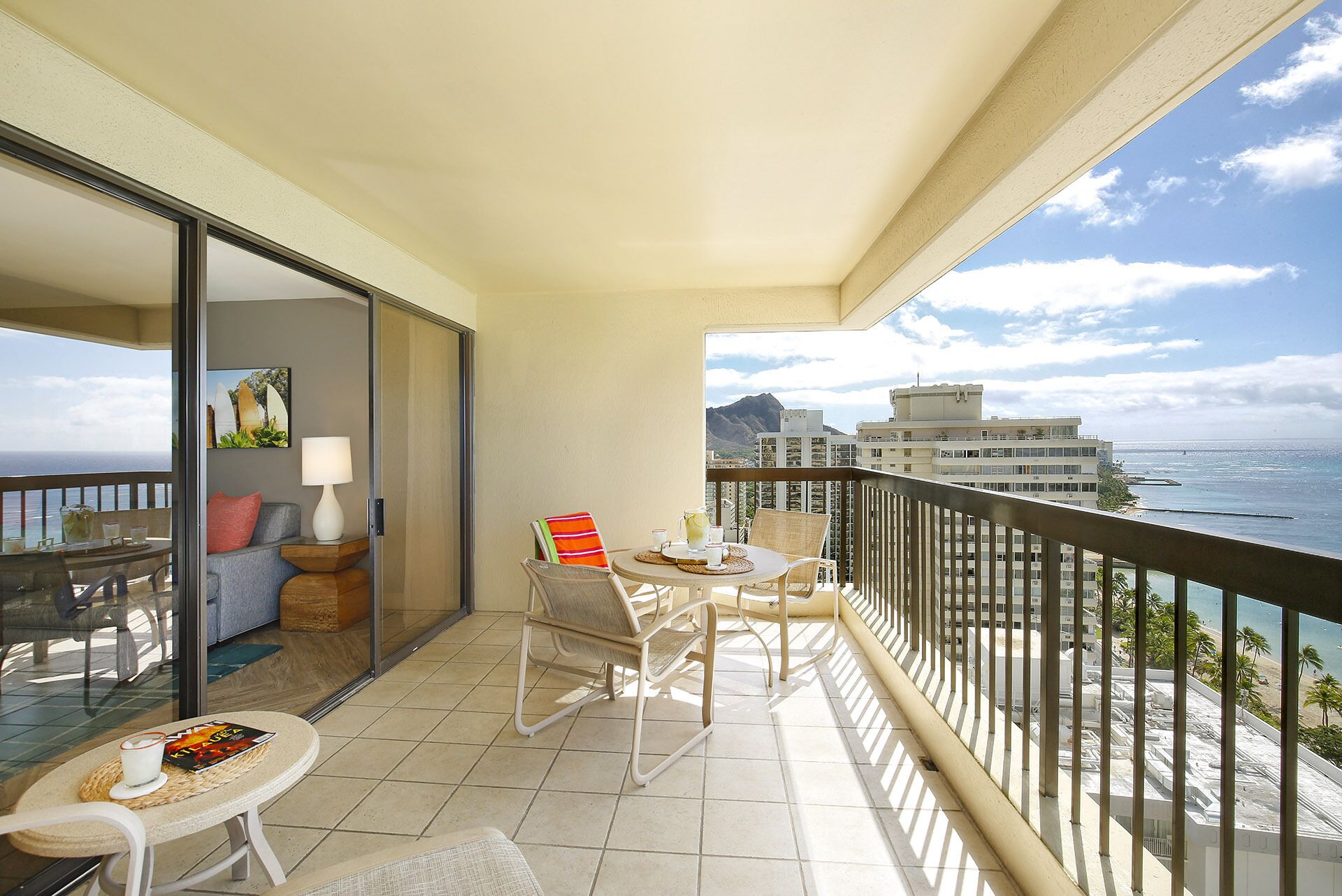 A balcony with a table and chairs, a sofa, and a view of the ocean and buildings.