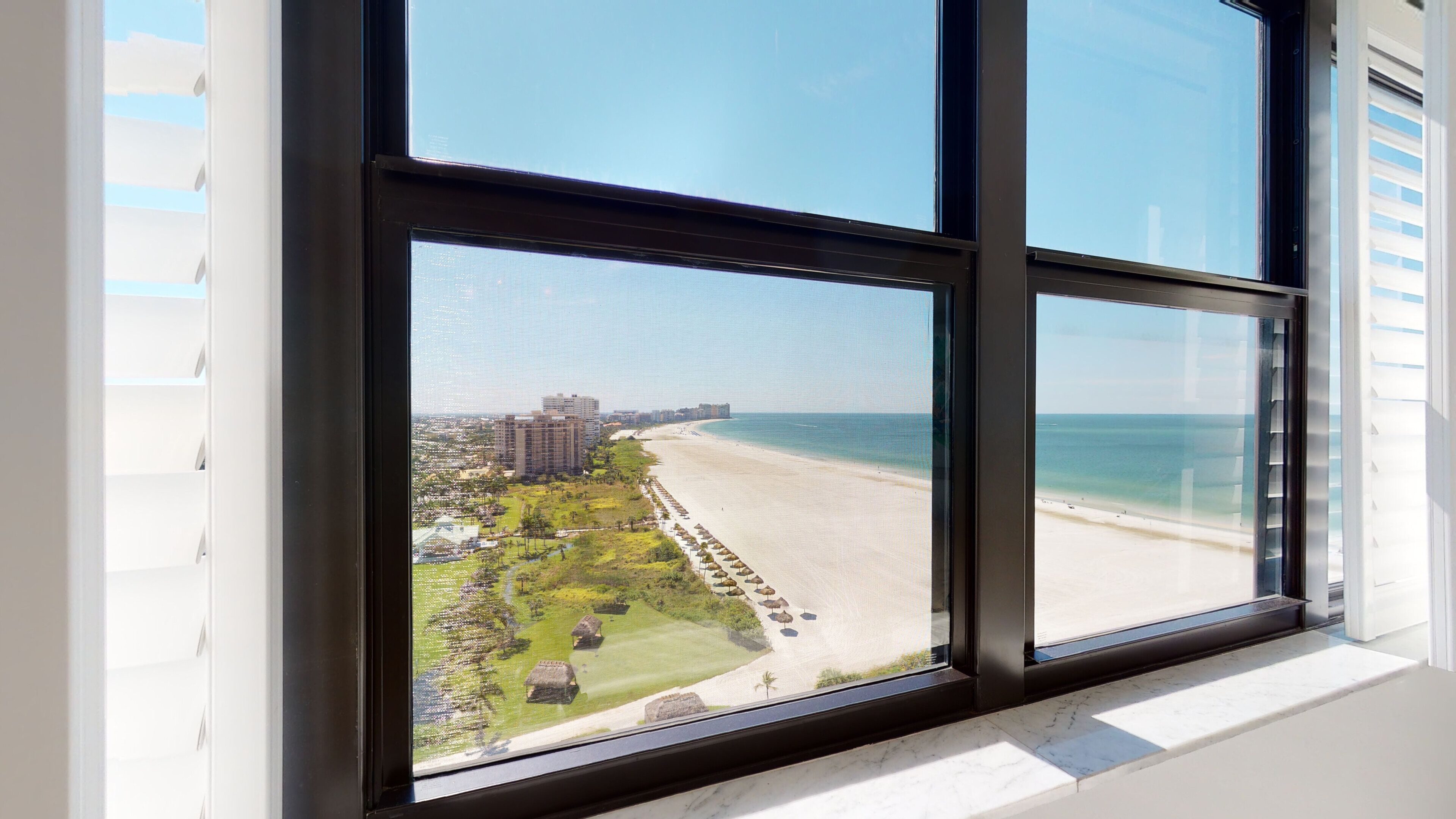 Vista desde una ventana hacia una playa, un campo de golf y edificios a lo lejos.