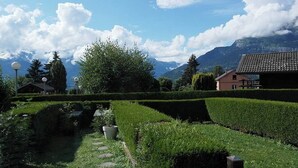Un jardin aménagé avec un sentier, un bâtiment doté d’un toit rouge et des montagnes en arrière-plan.